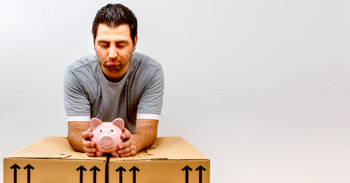 man leaning on moving boxes looking at savings